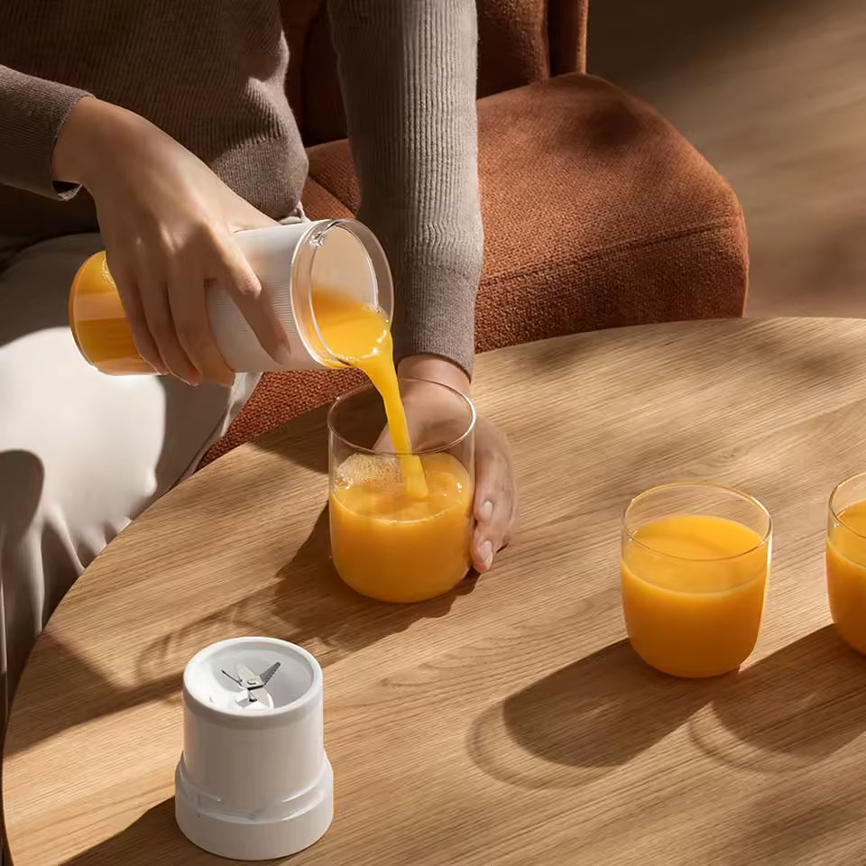 A person pouring a perfectly homogenized orange juice from the 300ML Alphinea portable blender into a glass on a wooden table, demonstrating the results of the 40-second rapid-squeeze technology.