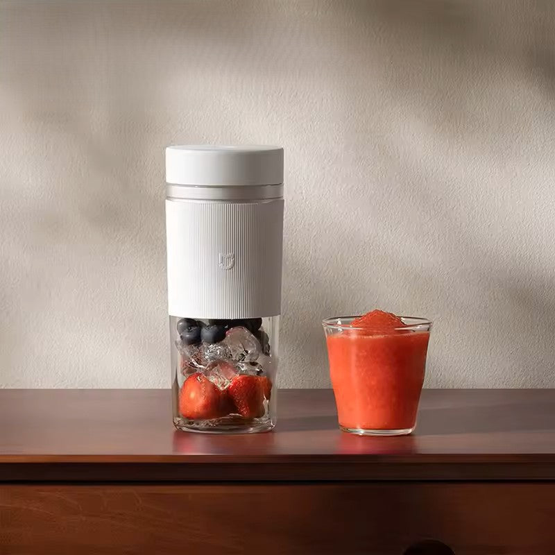 Alphinea portable blender filled with fresh strawberries, blueberries, and ice on a wooden counter, next to a glass of blended red smoothie. Highlights the clear, BPA-free PCTG vessel design.