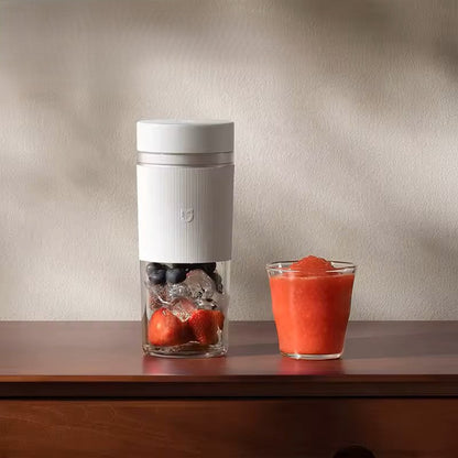 Alphinea portable blender filled with fresh strawberries, blueberries, and ice on a wooden counter, next to a glass of blended red smoothie. Highlights the clear, BPA-free PCTG vessel design.
