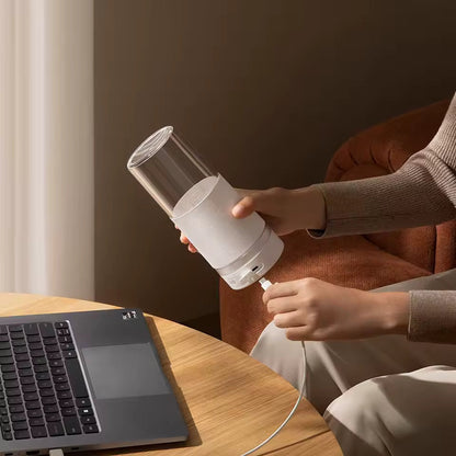 A person plugging a charging cable into the white Alphinea portable blender next to a laptop. Showcasing convenient on-the-go charging for fresh noon break office smoothies.