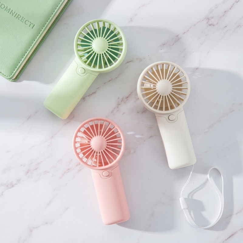 Three Alphinea creative handheld fans in pink, green, and white laid out on a marble surface