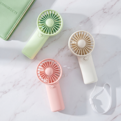 Three Alphinea creative handheld fans in pink, green, and white laid out on a marble surface