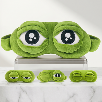 A studio display of the Alphinea 3D Frog Sleep Mask resting on a modern white surface, showing the main mask above three smaller versions that model the interactive open, winking, and closed eye features.