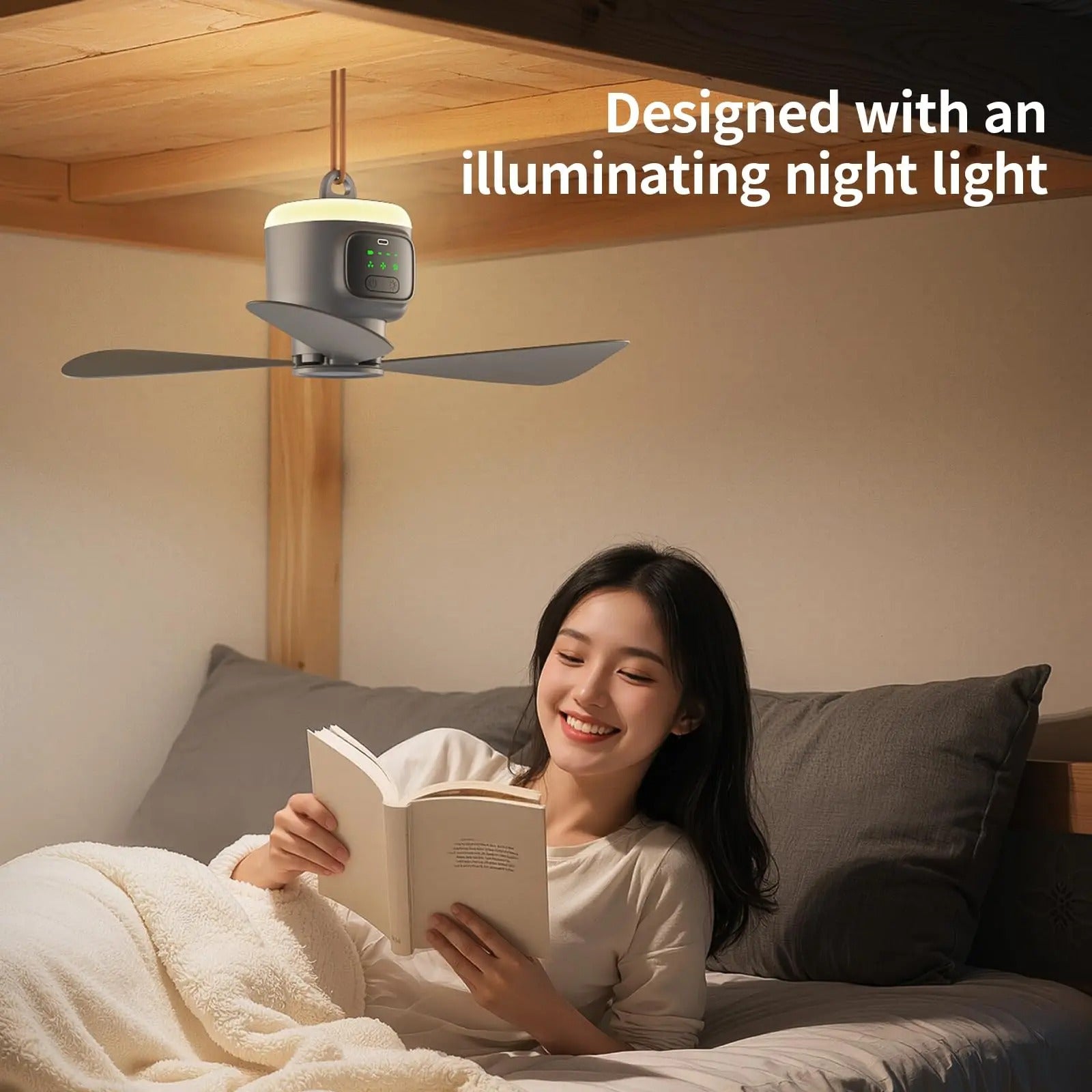 Une femme souriante lit un livre au lit, éclairée par la douce lumière de la veilleuse intégrée du ventilateur de plafond portable Alphinea suspendu au-dessus d'elle.