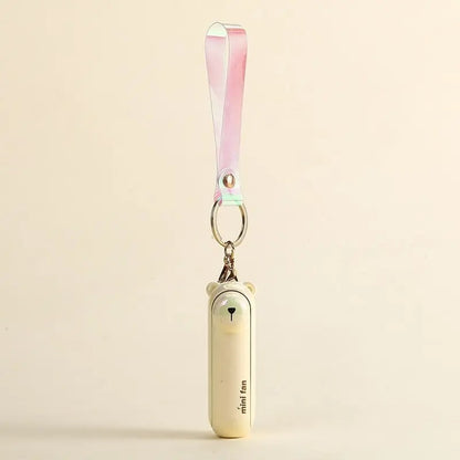 Cream bear design of the Alphinea foldable mini fan standing upright with its lanyard attached, displaying its compact size on a beige background.