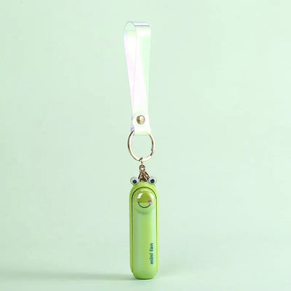 Green frog version of the Alphinea portable electric fan hanging by a white strap against a mint green background.